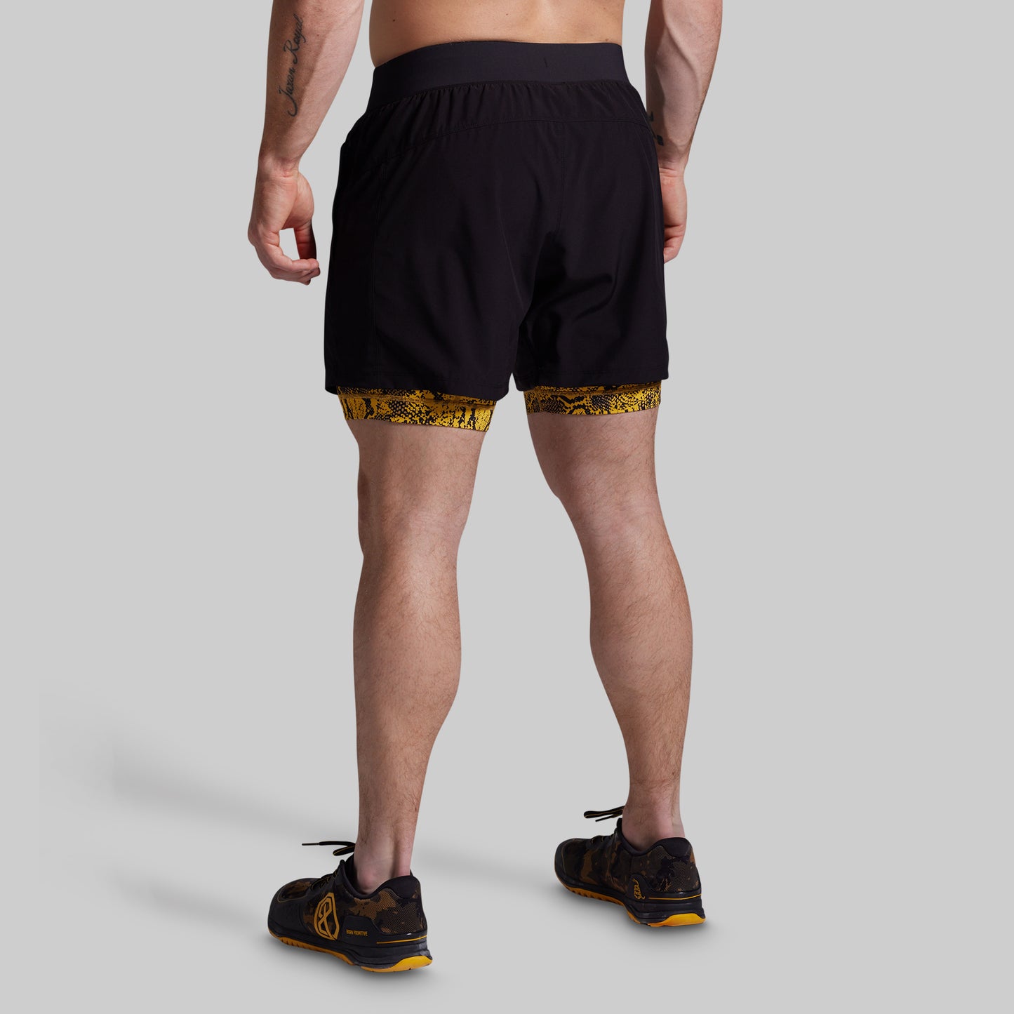 Person wearing black athletic shorts with a yellow pattern on a gray background