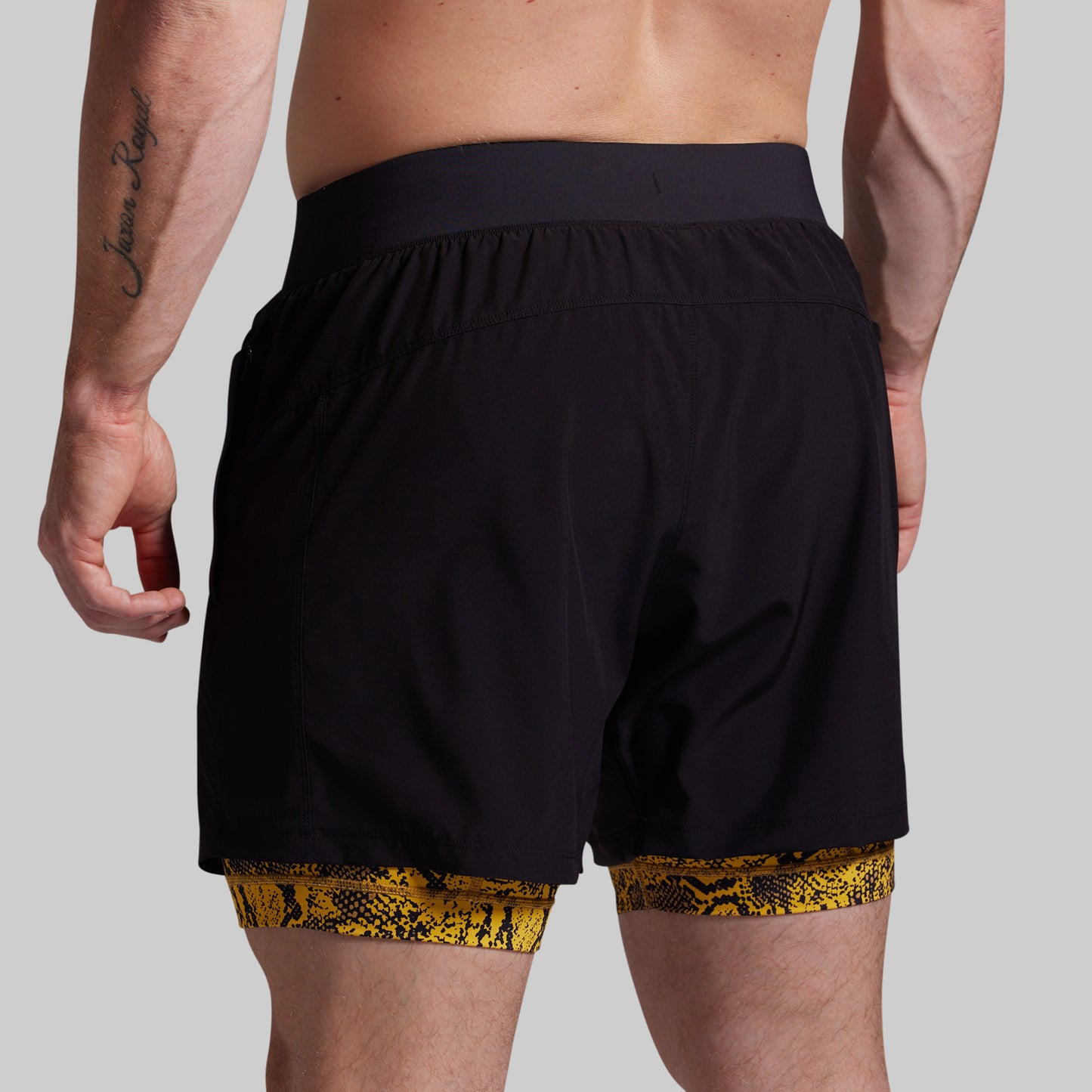 Person wearing black shorts with yellow snake print trim on a gray background