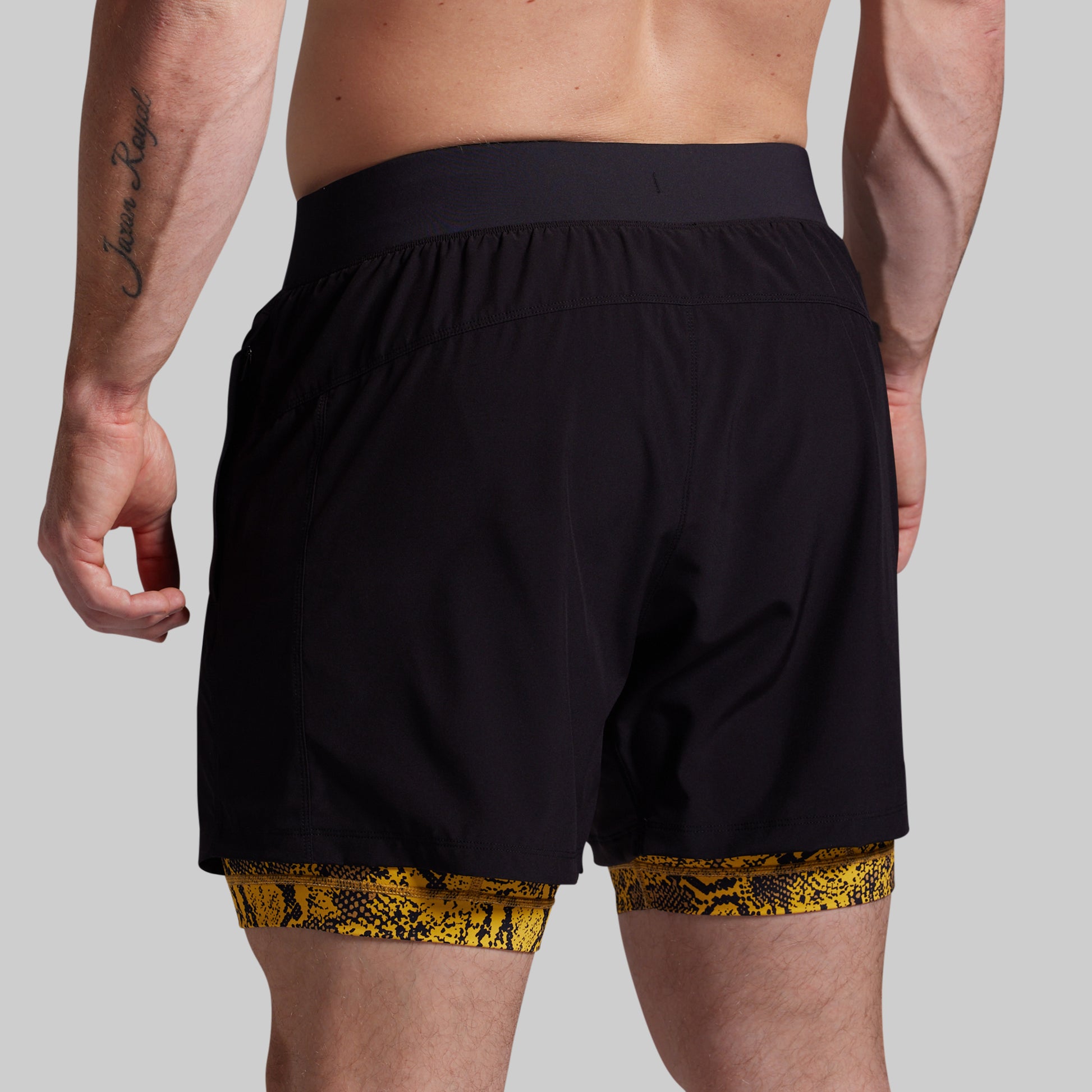 Person wearing black shorts with yellow snake print trim on a gray background
