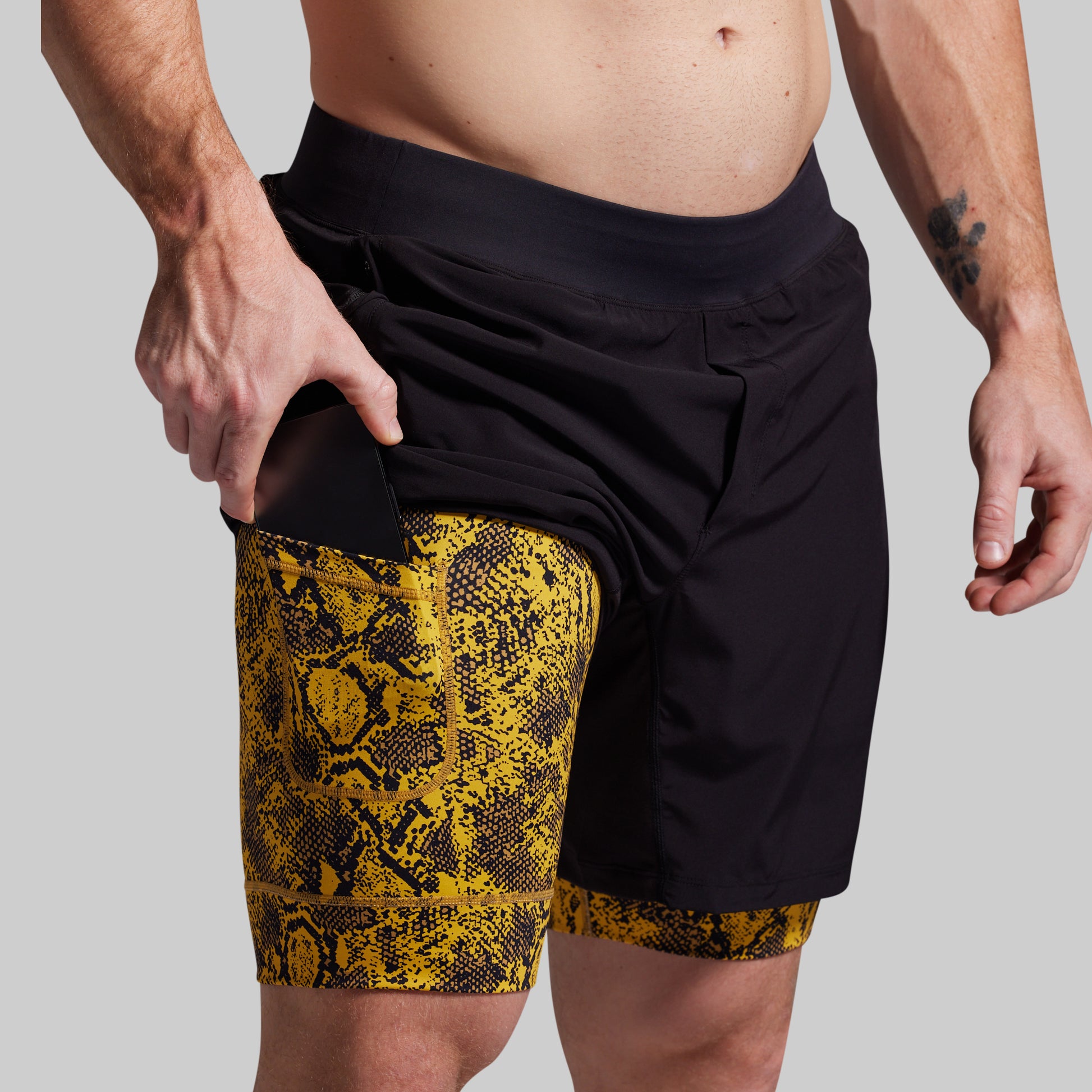 Person wearing black shorts with yellow snake print trim on a plain background