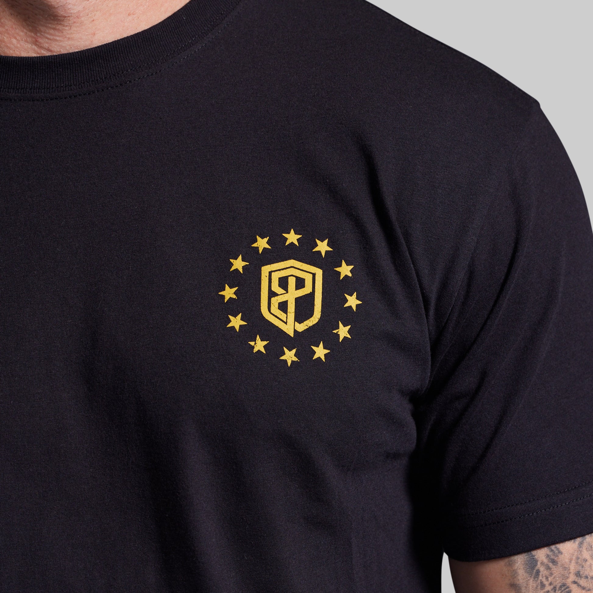 Black t-shirt with a yellow emblem featuring a shield and stars on a gray background