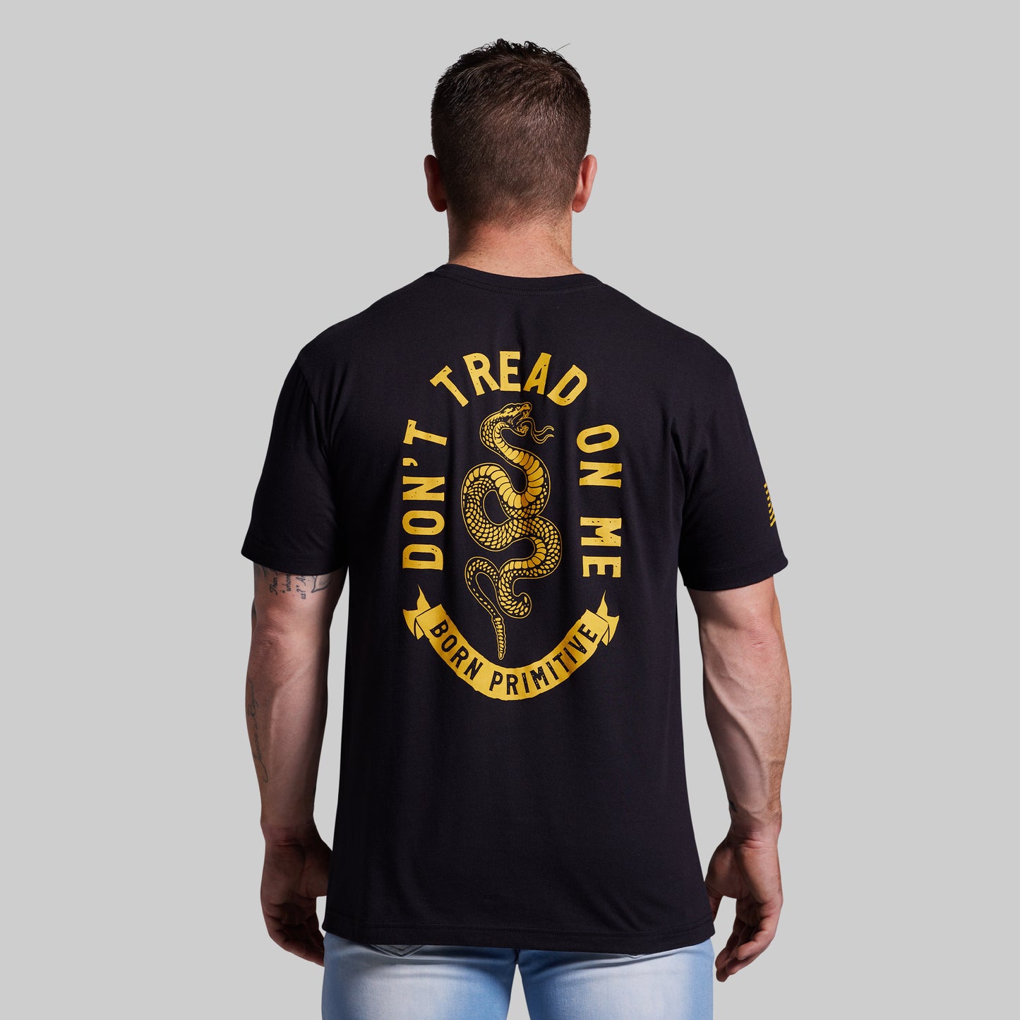 Man wearing a black t-shirt with 'Don't Tread on Me' graphic on the back against a gray background