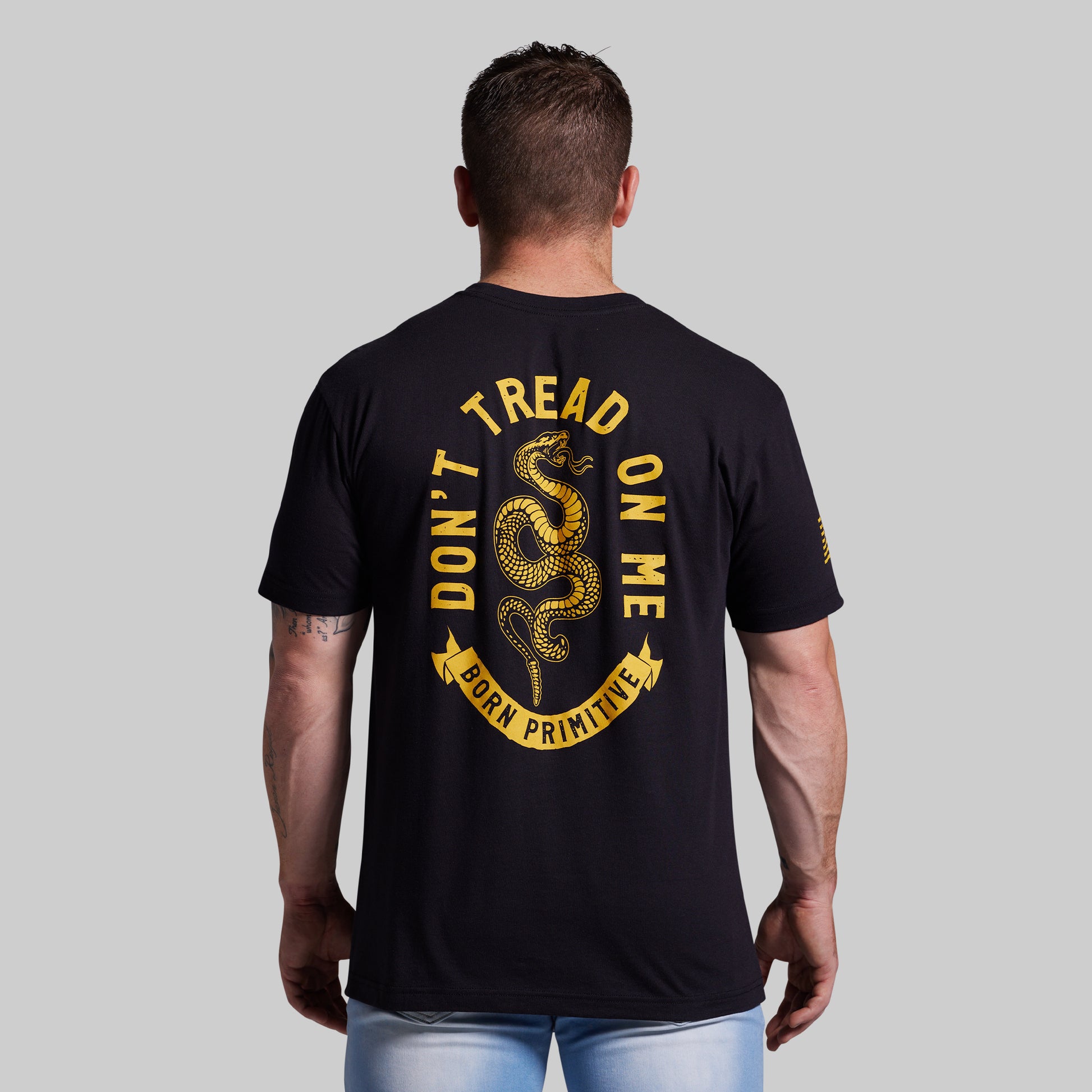 Man wearing a black t-shirt with 'Don't Tread on Me' graphic on the back against a gray background