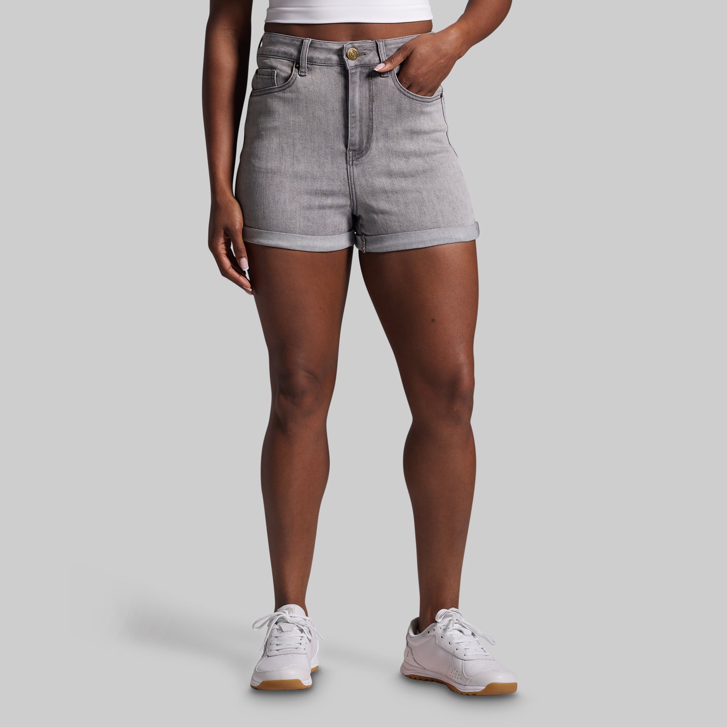 Person wearing gray shorts and white sneakers on a plain background
