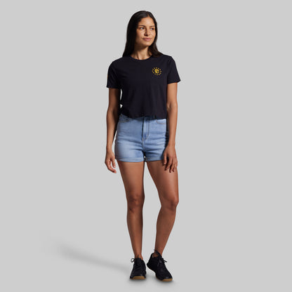 Woman wearing a black t-shirt with a yellow logo and denim shorts on a gray background