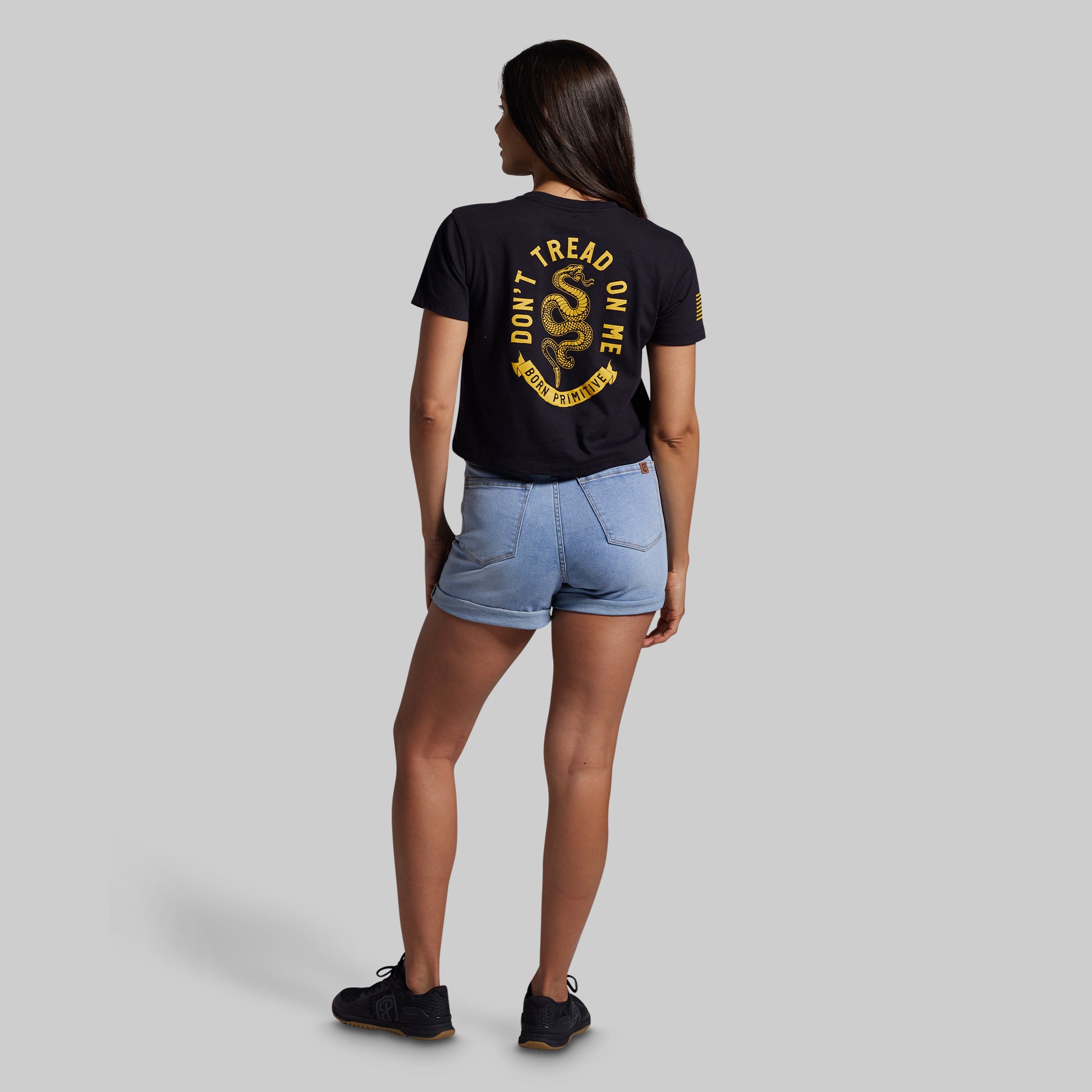 Person wearing a black t-shirt with yellow text and denim shorts on a gray background