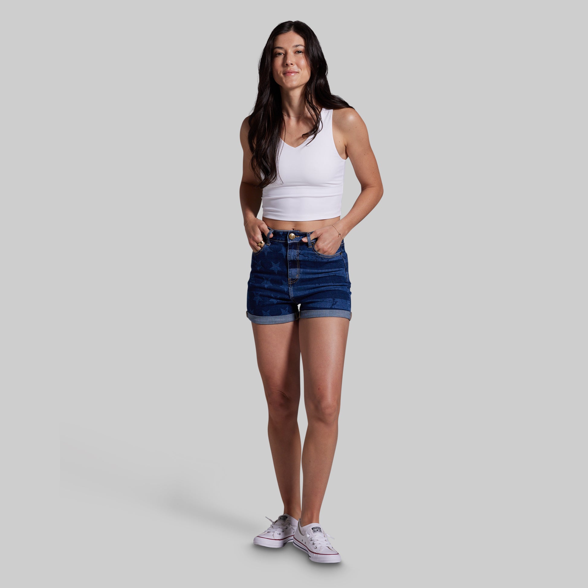 Woman wearing a white tank top and blue denim shorts on a gray background