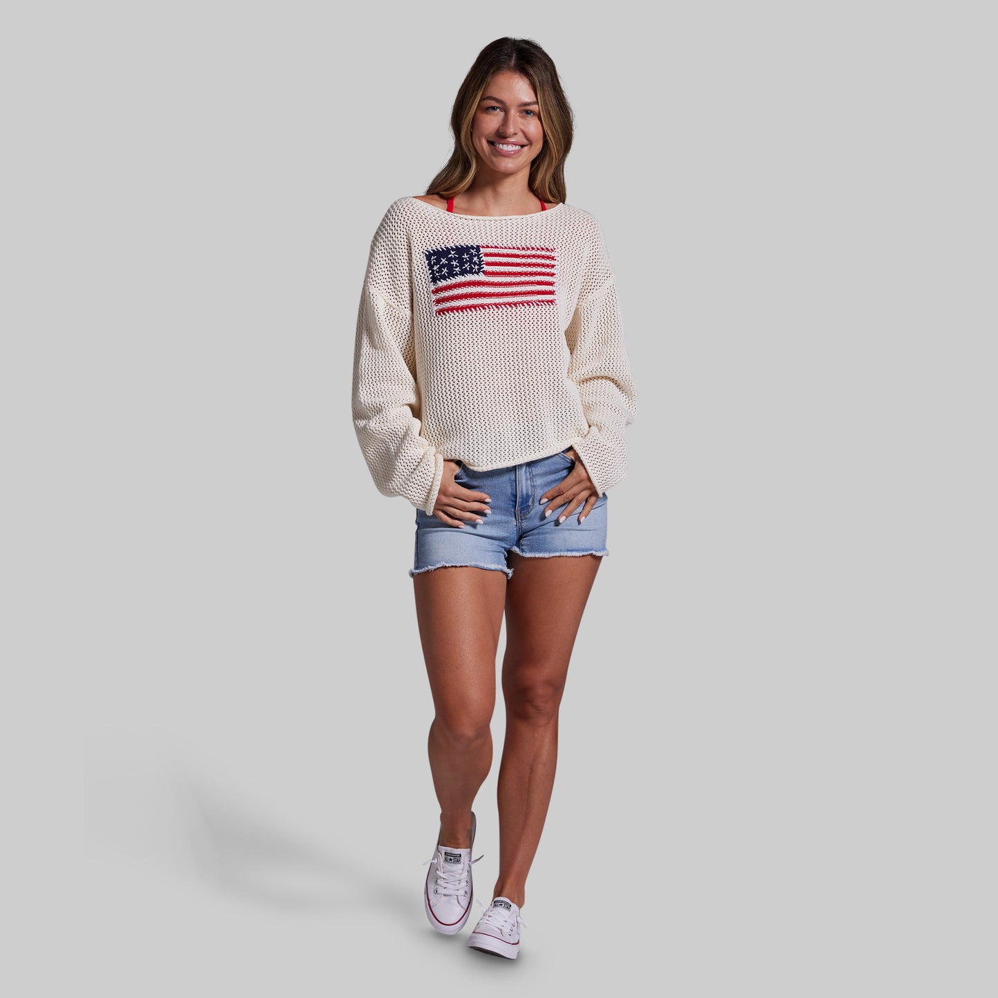 Woman wearing a cream sweater with an American flag design on a plain background
