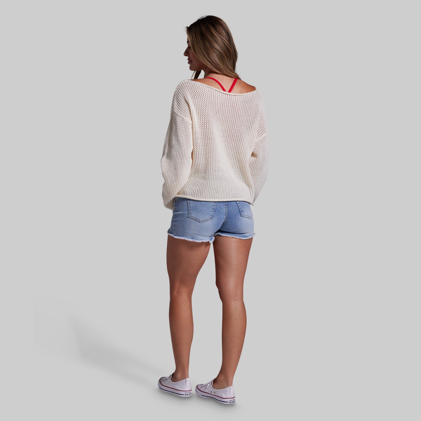 Woman wearing a beige sweater and denim shorts on a plain background