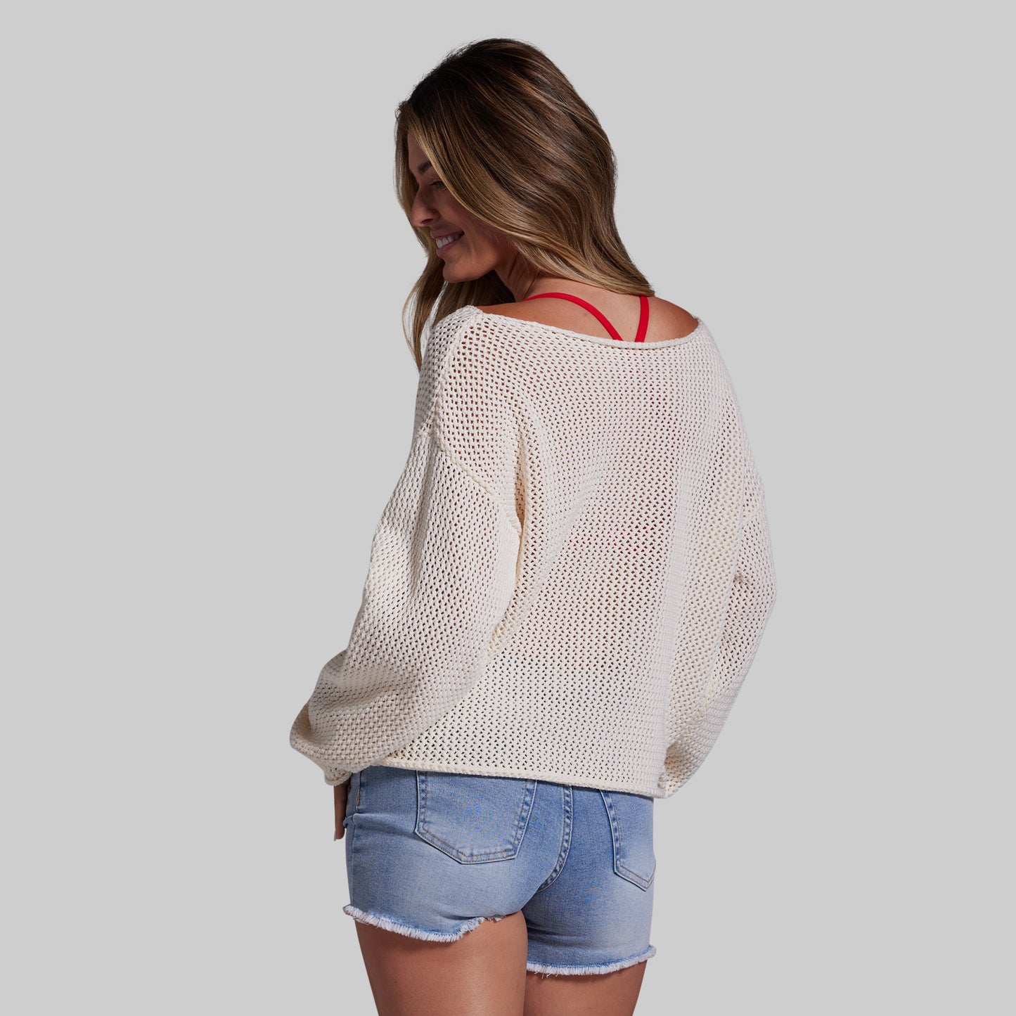 Woman wearing a beige sweater and denim shorts on a plain background
