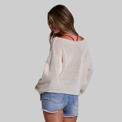 Woman wearing a beige sweater and denim shorts on a plain background