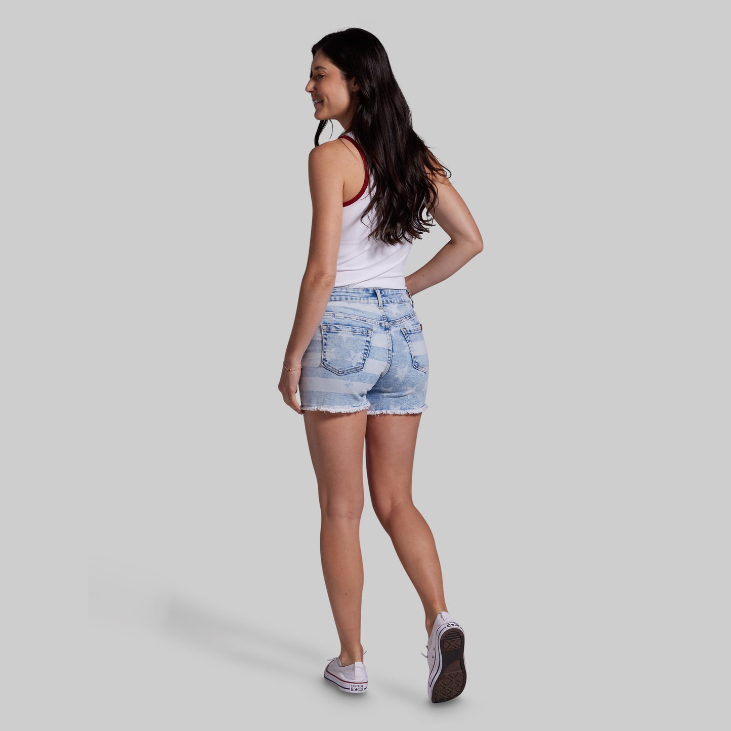 Woman wearing denim shorts and a white tank top on a plain background