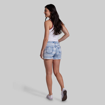 Woman wearing denim shorts and a white tank top on a plain background