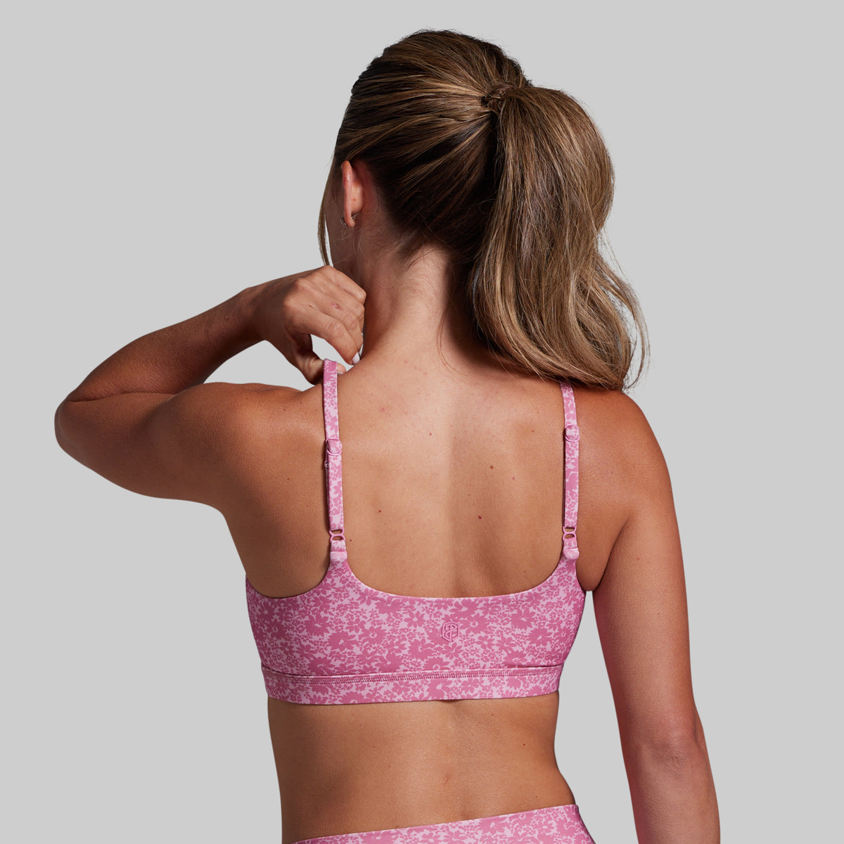 Woman wearing a pink sports bra and leggings against a gray background