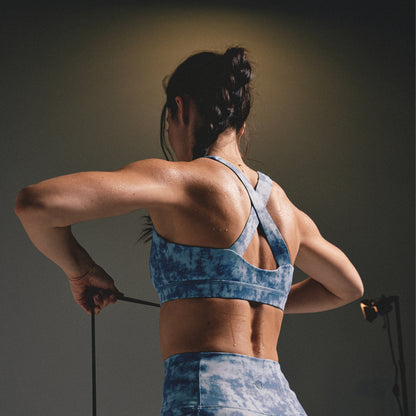 Woman in blue tie-dye athletic wear stretching against a dark background