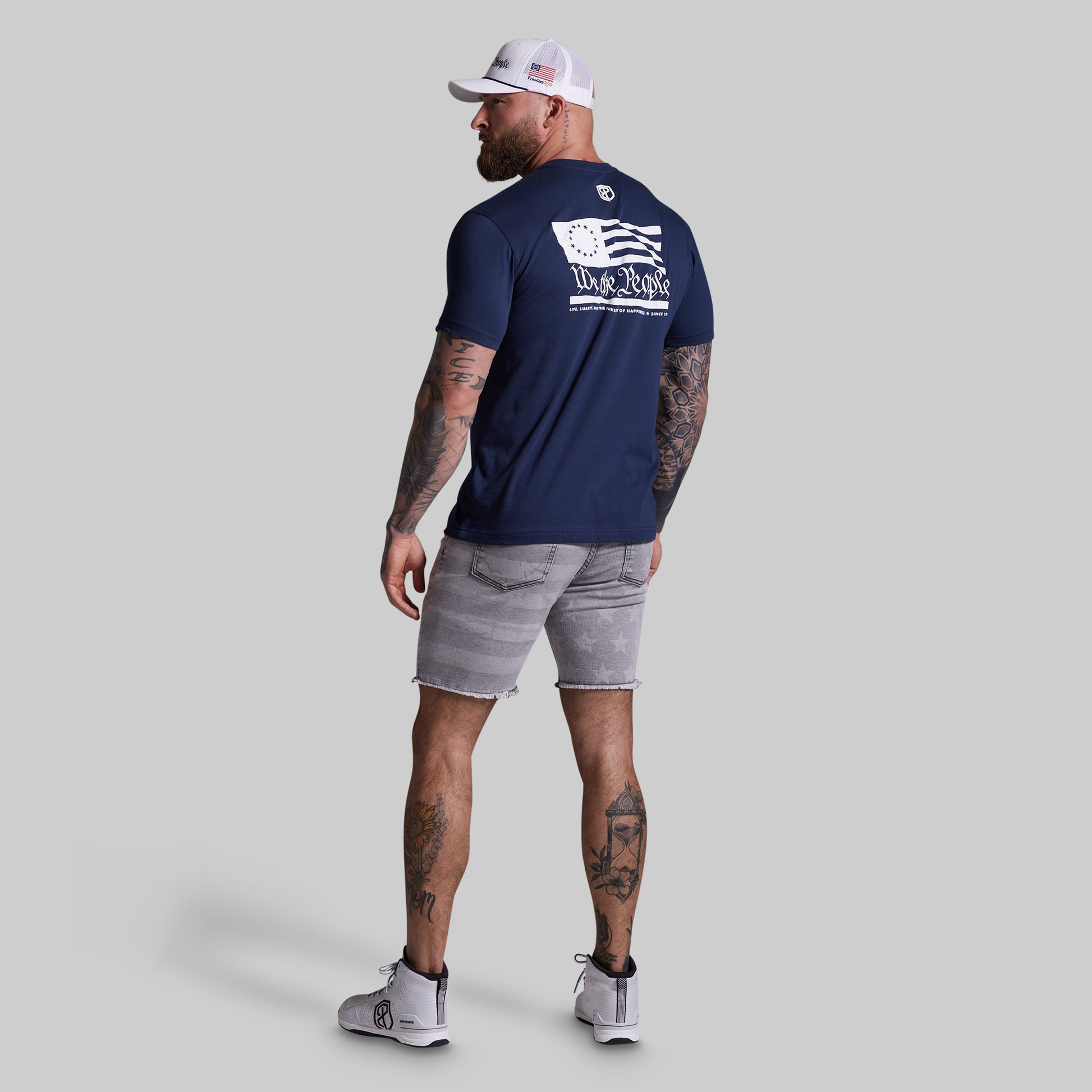 Man wearing a navy blue t-shirt with a logo on the back, standing against a gray background