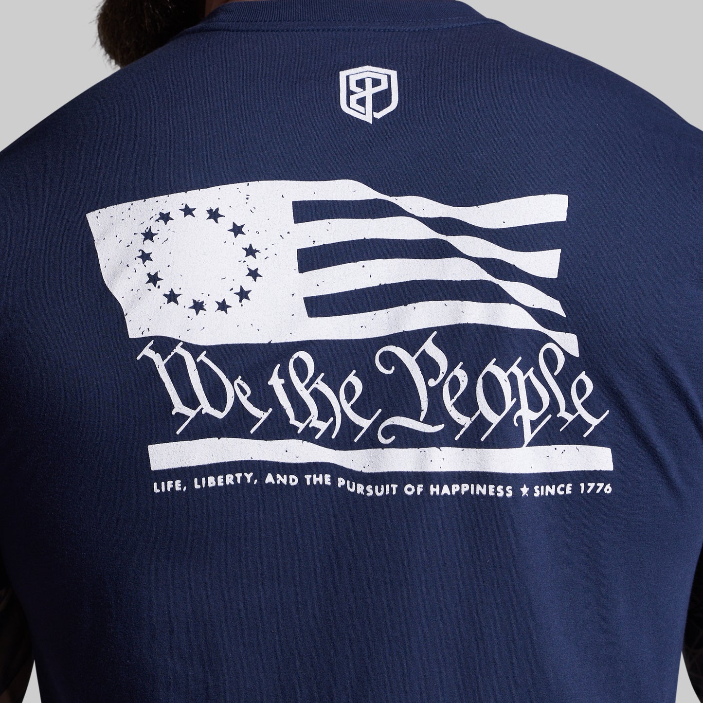 Navy blue shirt with white graphic of an American flag and text on the back, on a plain background.
