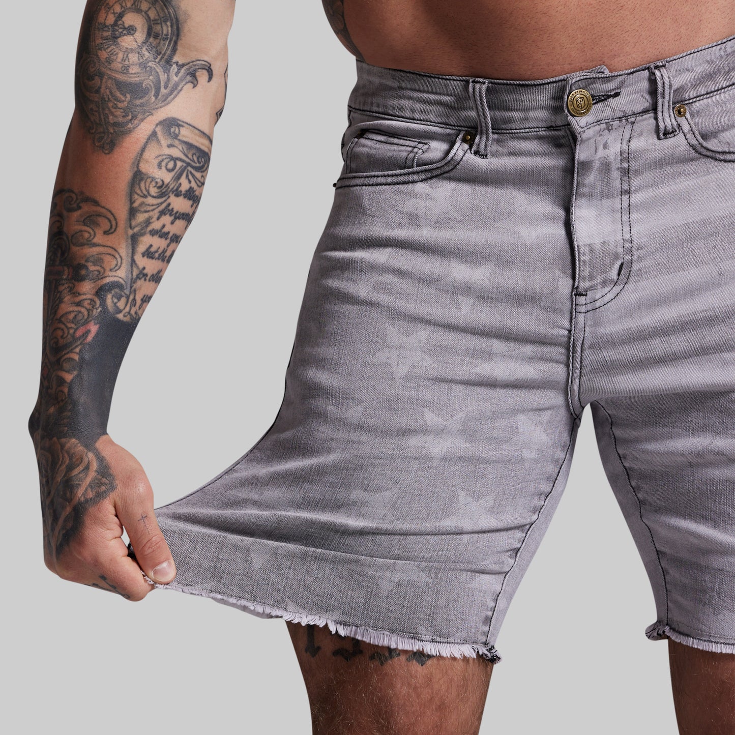 Person wearing gray denim shorts with visible tattoos on arm, on a plain background