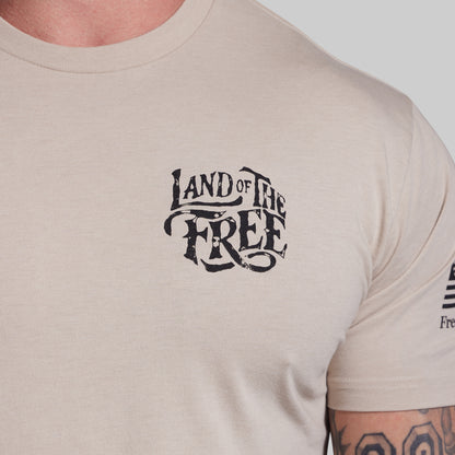 Beige t-shirt with 'Land of the Free' text on a plain background