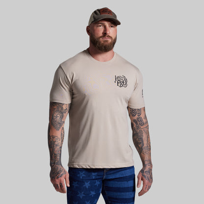 Man wearing a beige t-shirt with a logo and blue pants with star patterns on a gray background