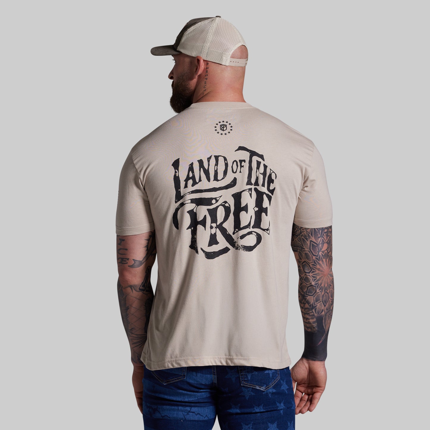 Man wearing a beige t-shirt with 'Land of the Free' text on the back, standing against a plain background.