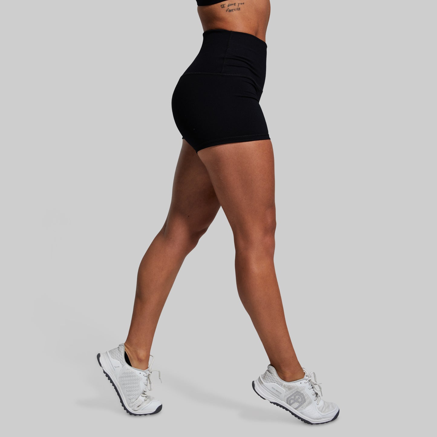 Person wearing black high-waisted shorts and white sneakers on a gray background