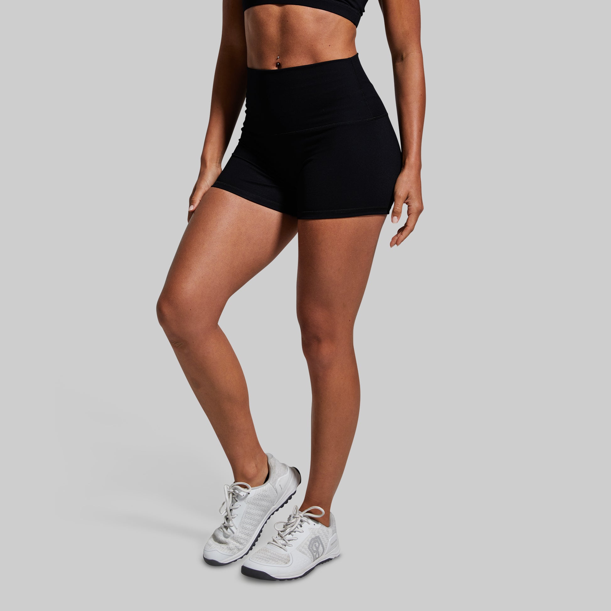 Person wearing black athletic shorts and white sneakers on a gray background