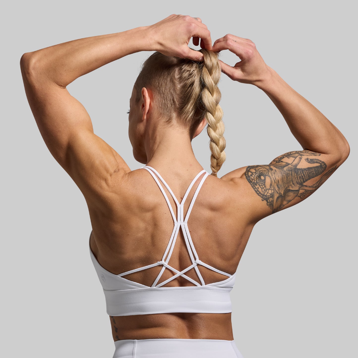 Person wearing a white sports bra with criss-cross straps against a gray background