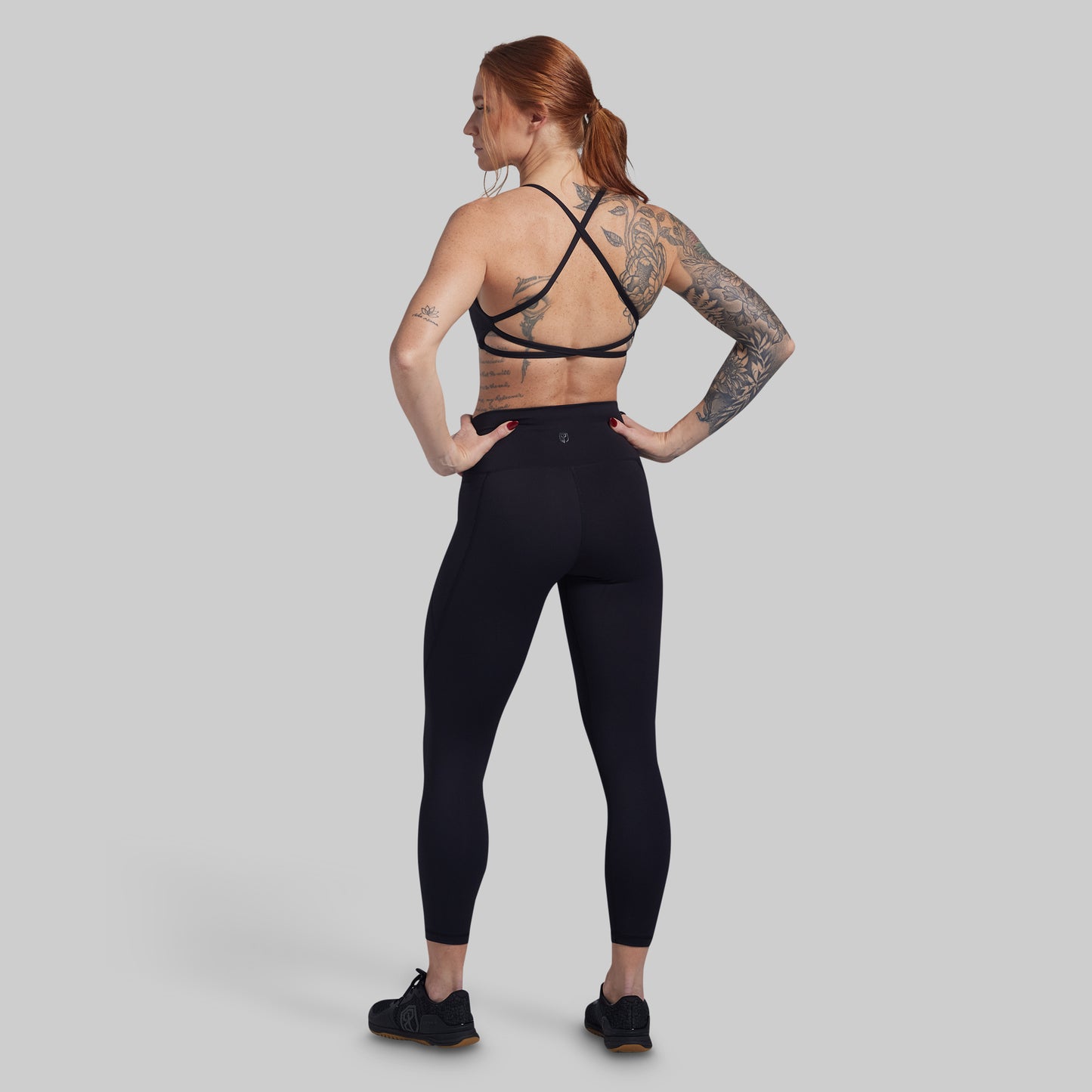 Person wearing black athletic leggings and sports bra on a gray background
