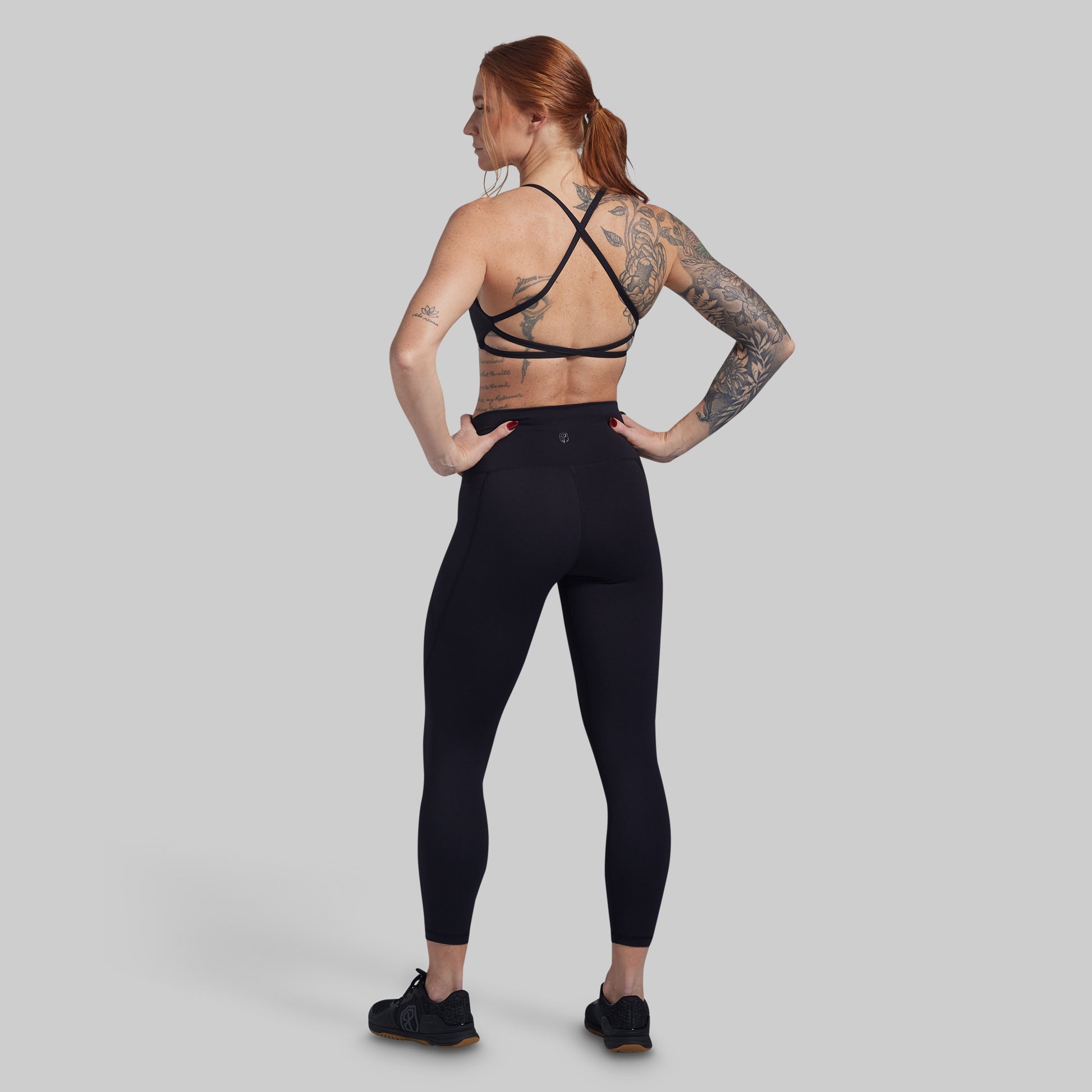 Person wearing black athletic leggings and sports bra on a gray background