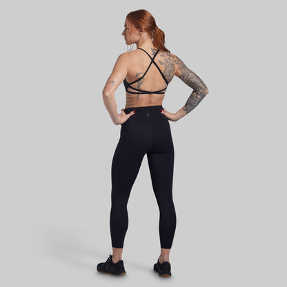 Person wearing black athletic leggings and sports bra on a gray background
