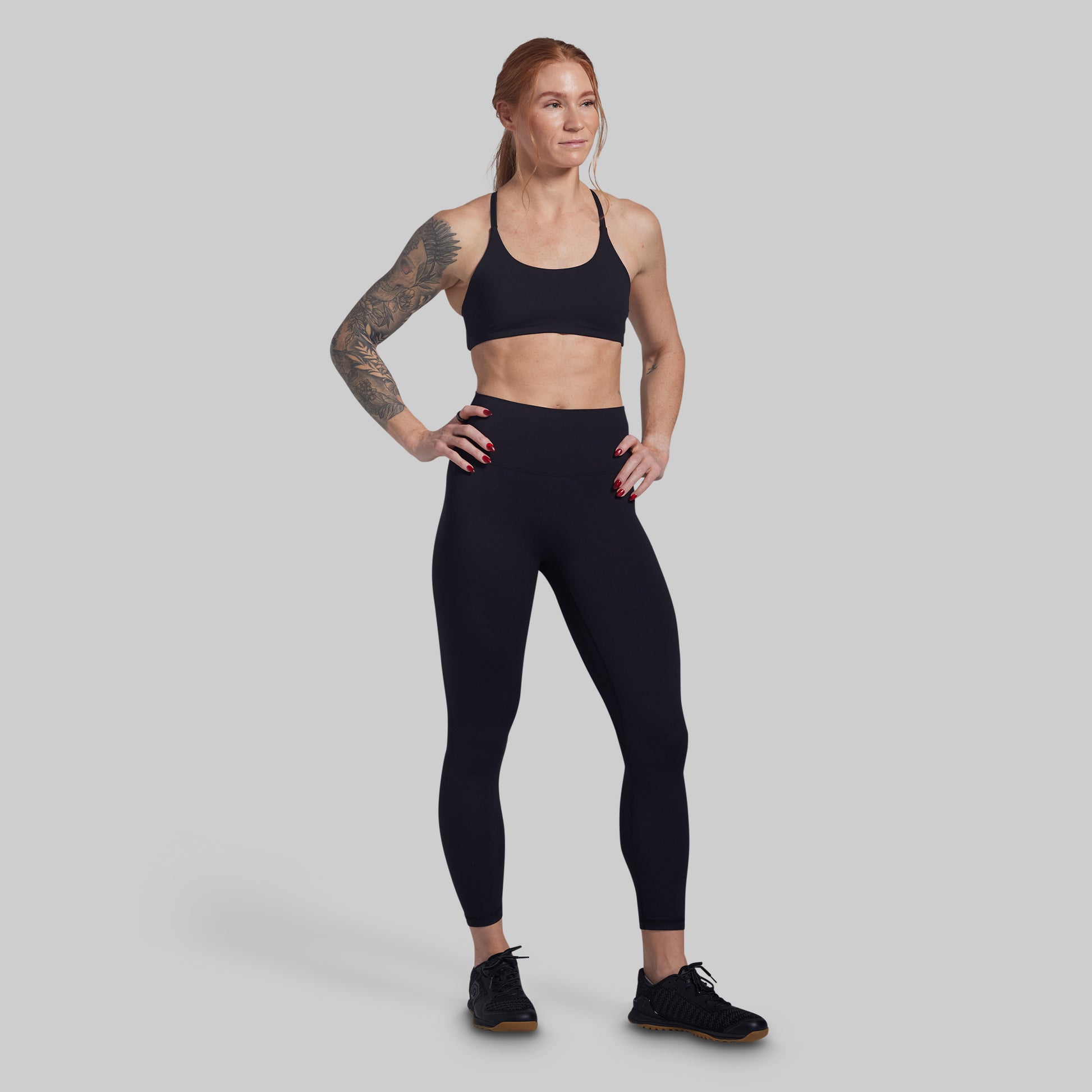 Woman wearing a black sports bra and leggings on a gray background