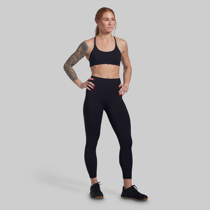 Woman wearing a black sports bra and leggings on a gray background