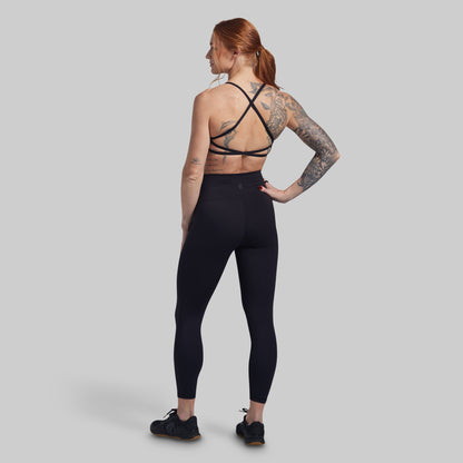 Person wearing black leggings and a strappy sports bra on a plain background