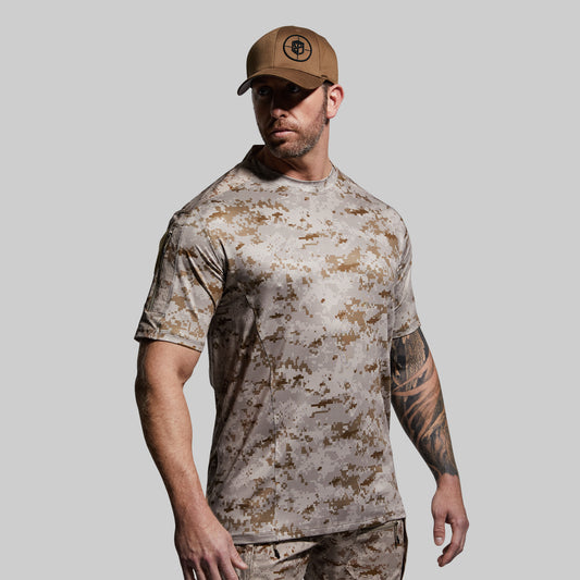 Man wearing a camouflage t-shirt and pants with a brown cap on a gray background