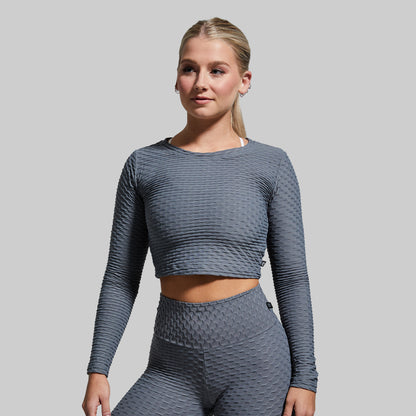 Woman wearing a gray textured long-sleeve top and leggings on a light gray background