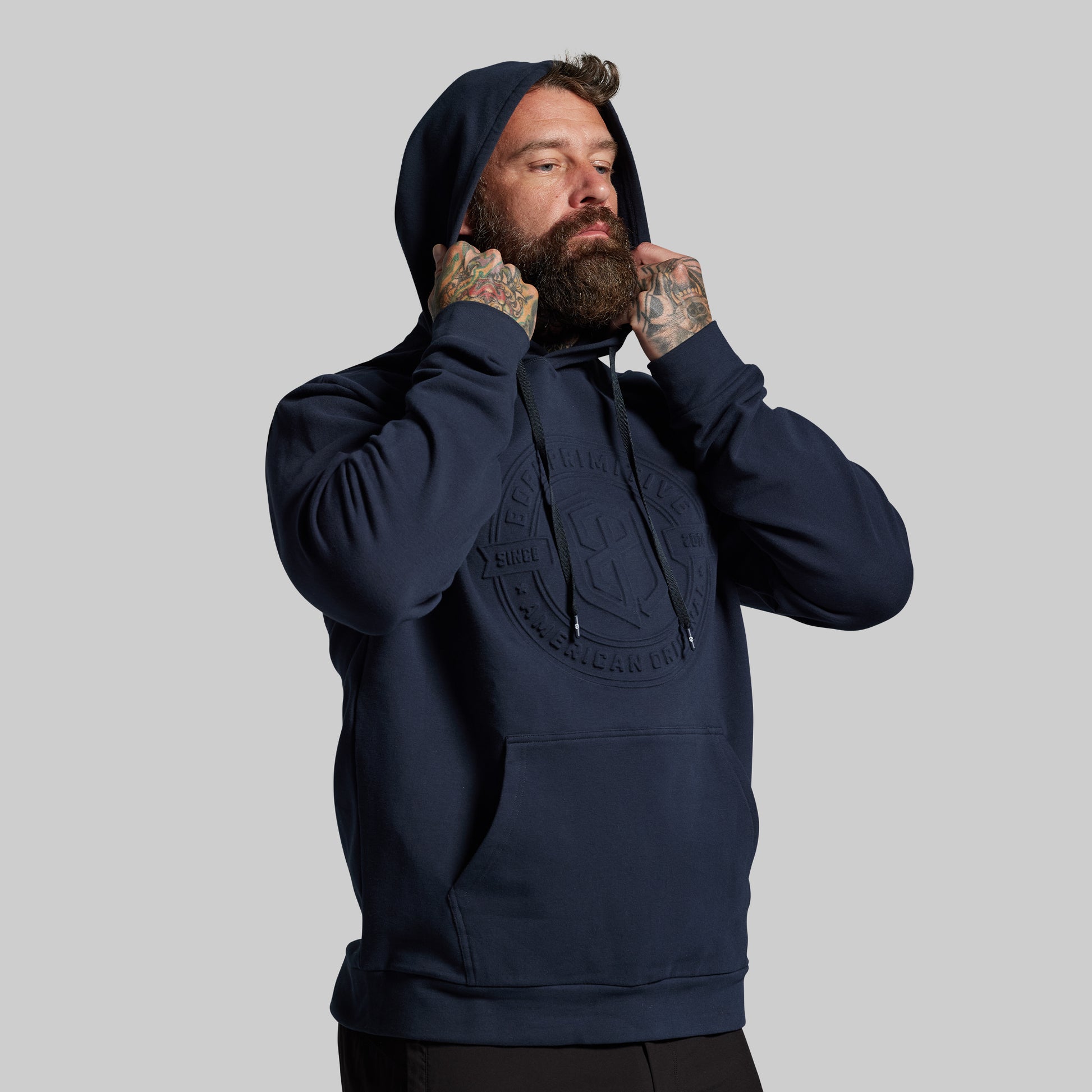 Man wearing a navy blue hoodie with a logo on a gray background