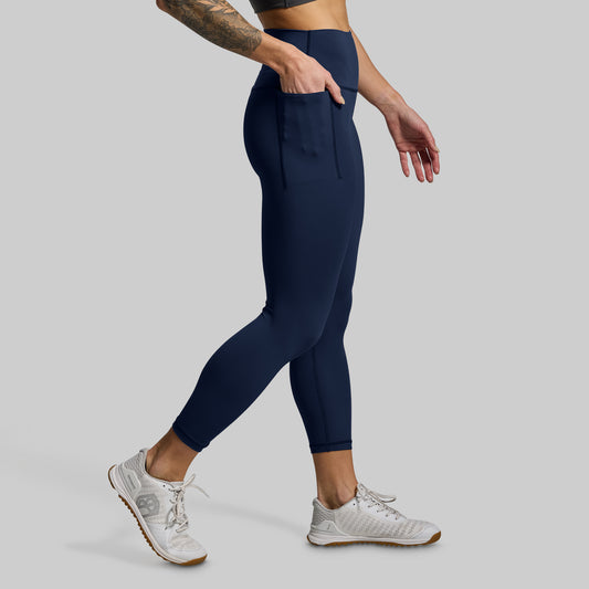 Person wearing navy leggings and white sneakers on a gray background