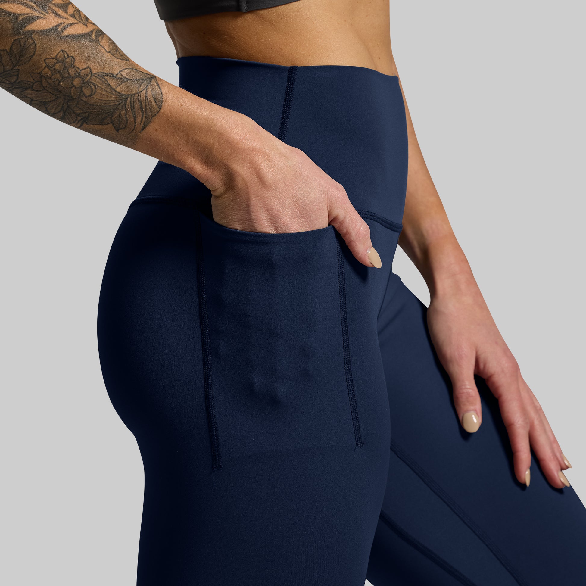 Person wearing a pair of blue leggings with hand in pocket on a gray background
