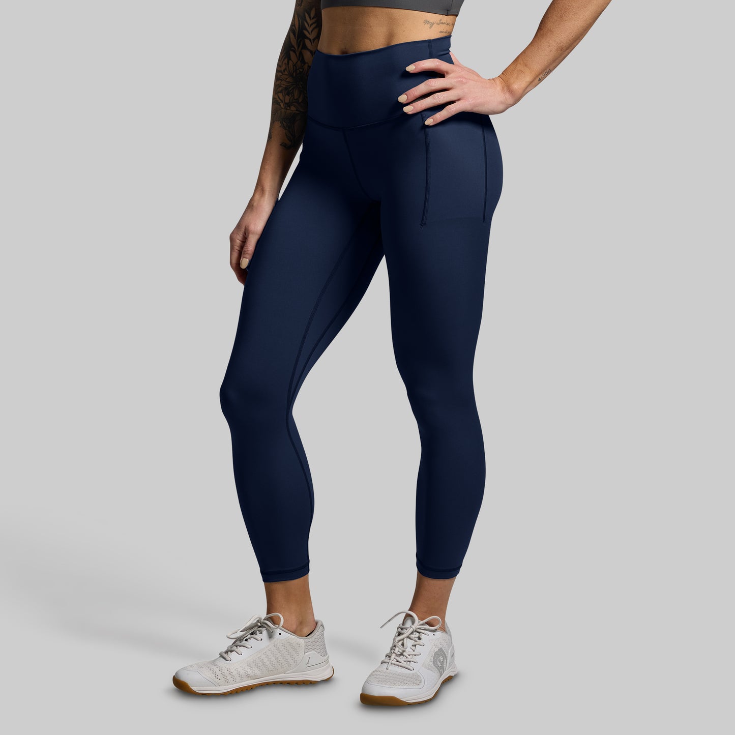 Person wearing dark blue leggings with pockets on a light gray background
