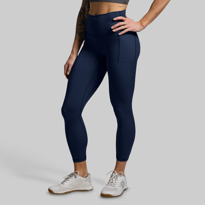 Person wearing dark blue leggings with pockets on a light gray background