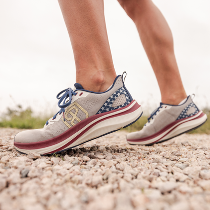 Person wearing red, white, and blue running shoes on a gravel path.