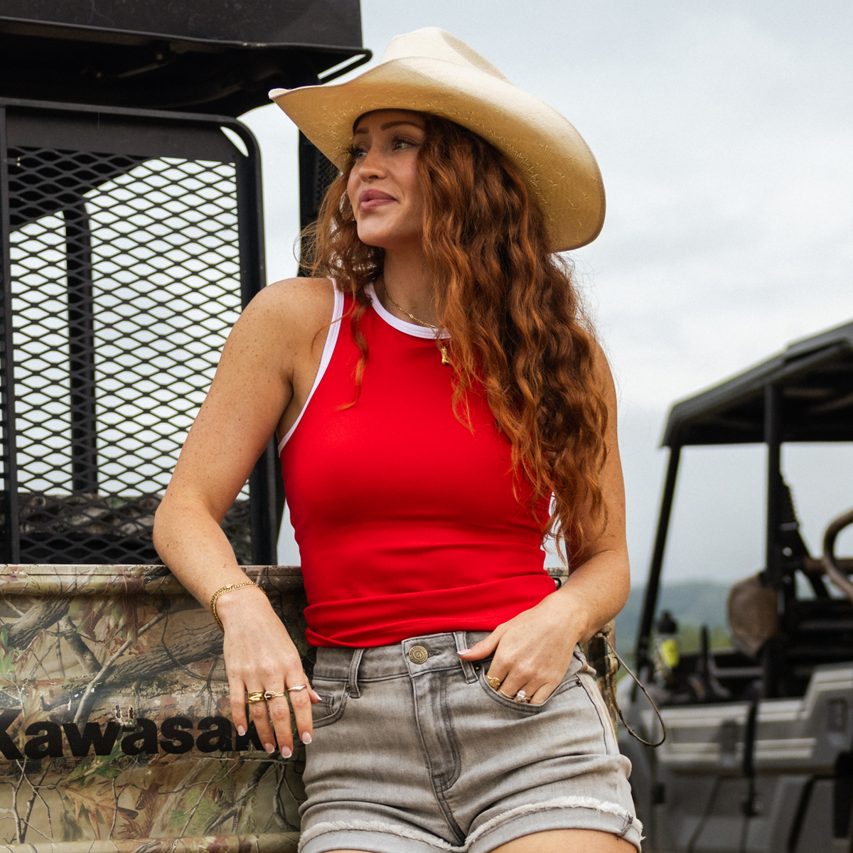 Woman wearing a red tank top and cowboy hat standing next to a Kawasaki vehicle.