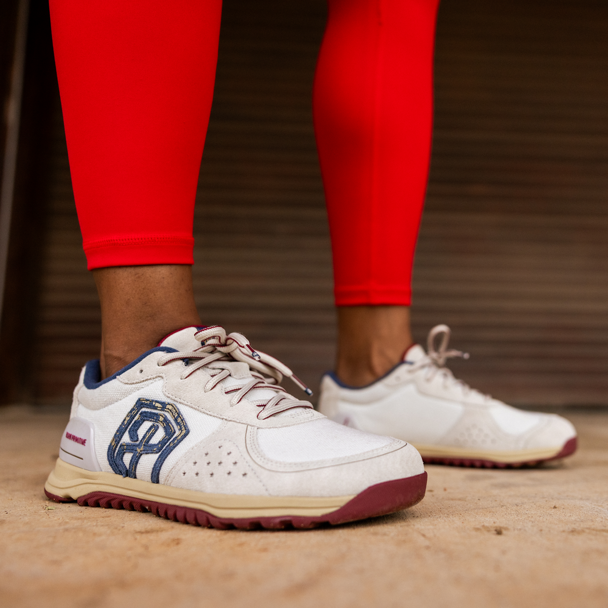White sneakers with blue accents worn with red leggings on a wooden floor.