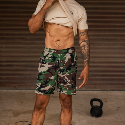 Man wearing camouflage shorts with a kettlebell on the ground, against a brown background
