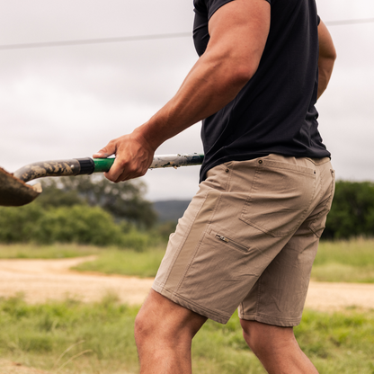 Person wearing beige shorts and a black shirt holding onto a shovel in an outdoor setting