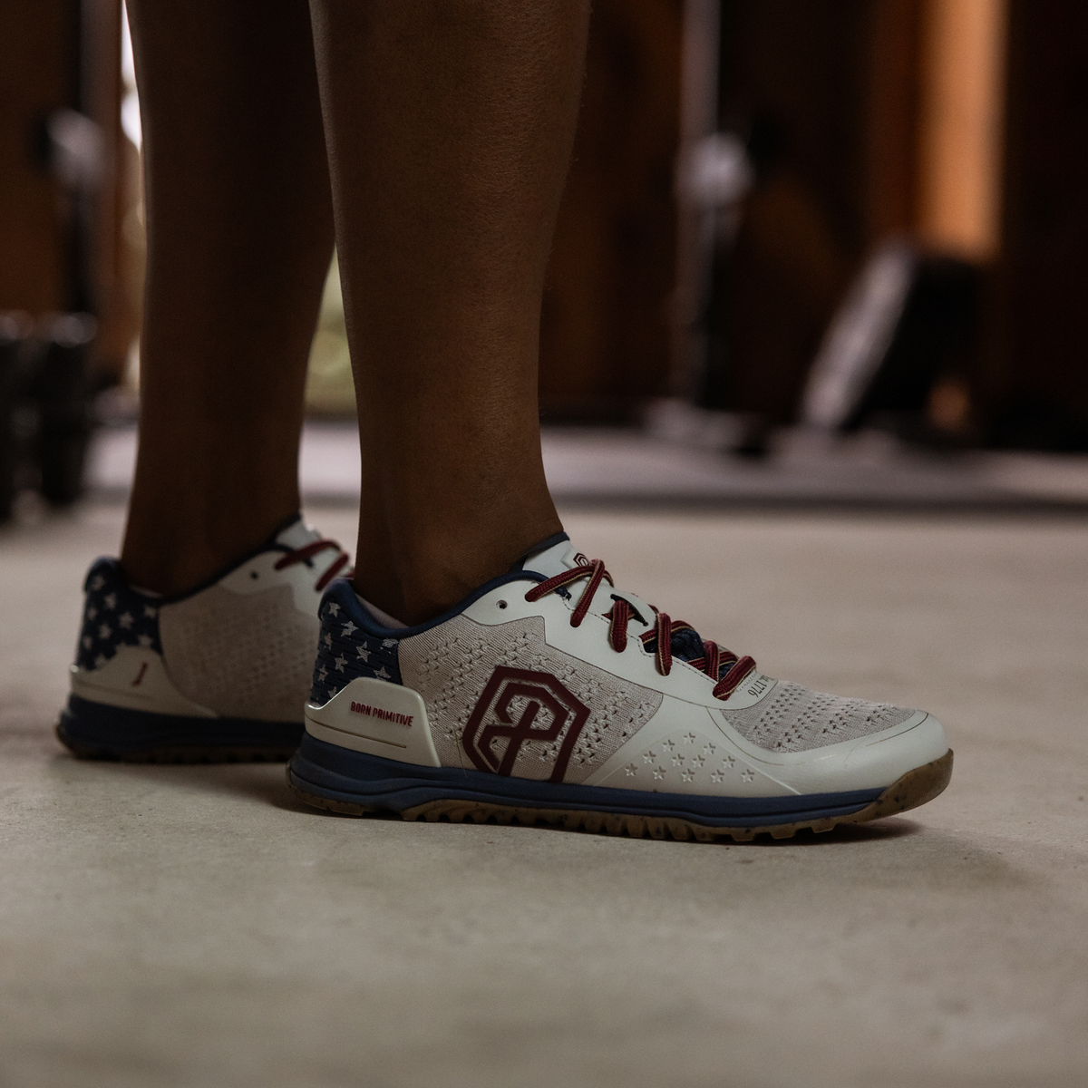 Close-up of white athletic shoes with red and blue accents on a blurred gym floor background.