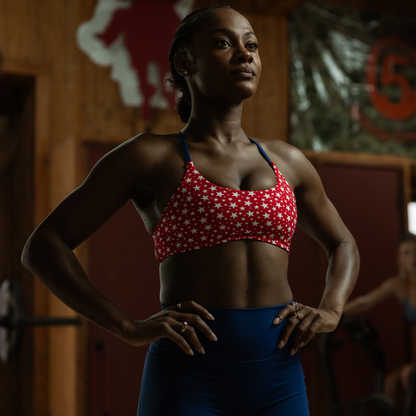Woman in a red and white sports bra with stars and blue leggings standing in a gym.