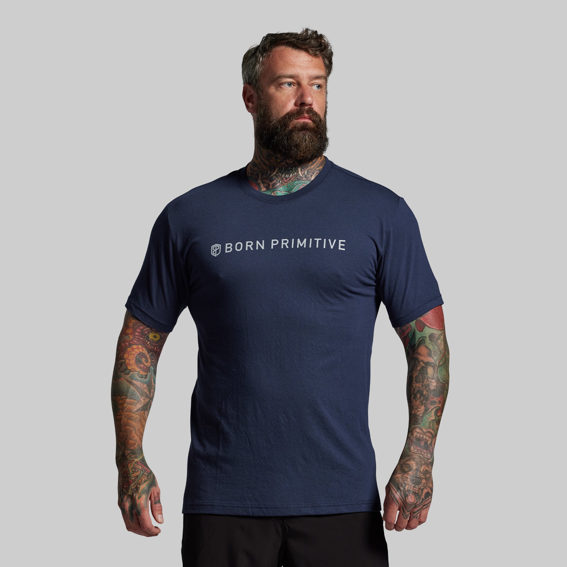 Man wearing a navy blue 'Born Primitive' t-shirt on a gray background