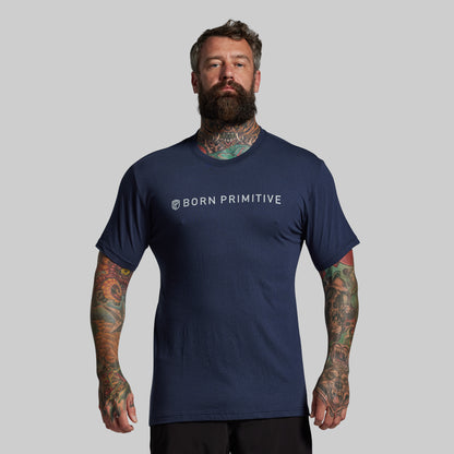 Man wearing a navy blue 'Born Primitive' t-shirt on a gray background